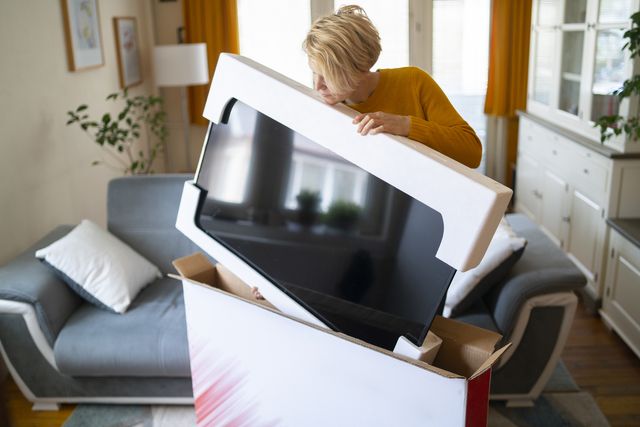 after online shopping at home during lockdown a woman takes delivery of her new smart tv, lifting it carefully from its protective wrapping inside her modern home