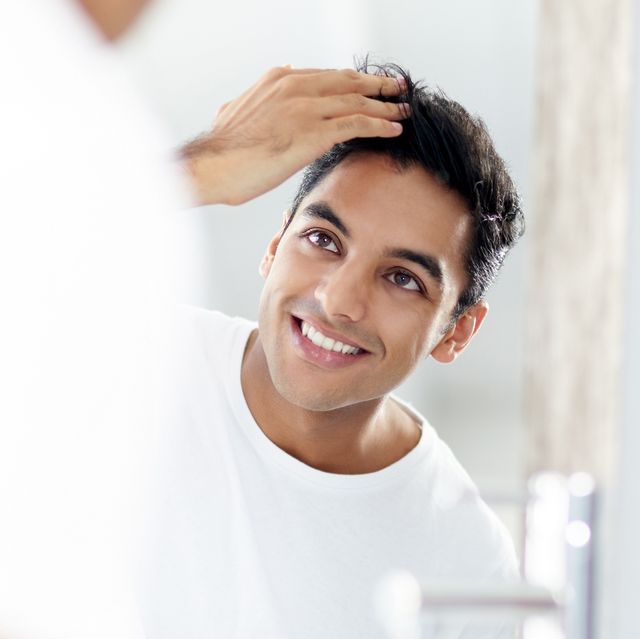 un hombre se toca el pelo delante del espejo