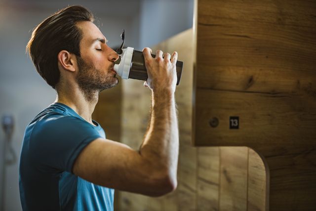 profile view of athletic man drinking water in a gym's locker room