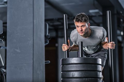 Athletic young man exercising with weight sled at gym