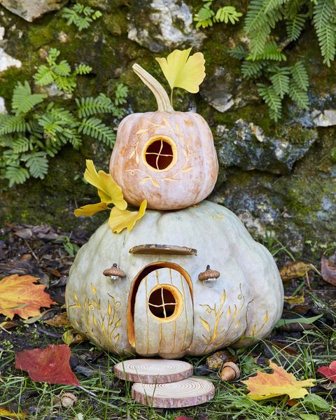 two stacked pumpkins decorated and carved to look like a gnome house, with sliced wood rounds as stepping stones