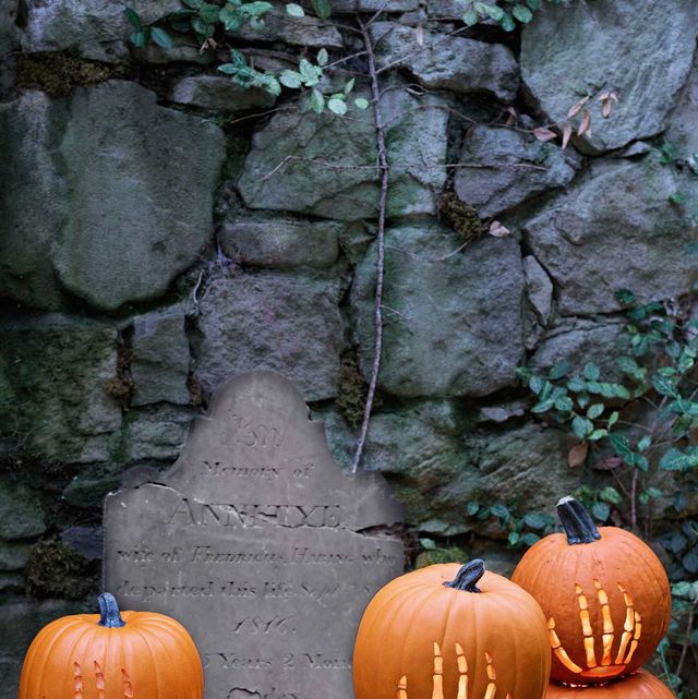 stacked pumpkins with hand and arm skeleton carvings in front of spooky cracked gravestone and old stone wall