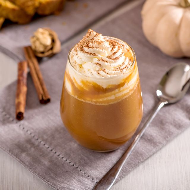 warm pumpkin drink with whipped cream and cinnamon sticks in glass cup with spoon