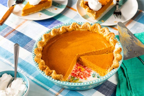 pumpkin pie recipe in a teal pie plate on a plaid table cloth with a green linen two slices of pie in the background with whipped cream