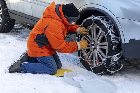 man in orange jacket placing chains over his front tires