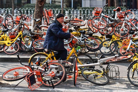 topshot   a man rides past shared bicycles piled beside a road in beijing on february 21, 2018china issued national guidelines governing bike sharing operations in 2017 in an effort to nurture a new industry credited with spurring a transport revolution while addressing mounting complaints over an accumulation of millions of bikes on city streets  afp photo  greg baker