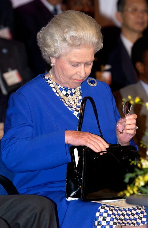 queen looks down into her purse, holding a pair of glasses