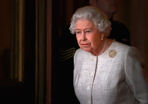 the queen stands in pearls and a beige jacket with gold brooch