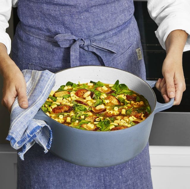 person holding a white bean and sausage stew in blue dutch oven