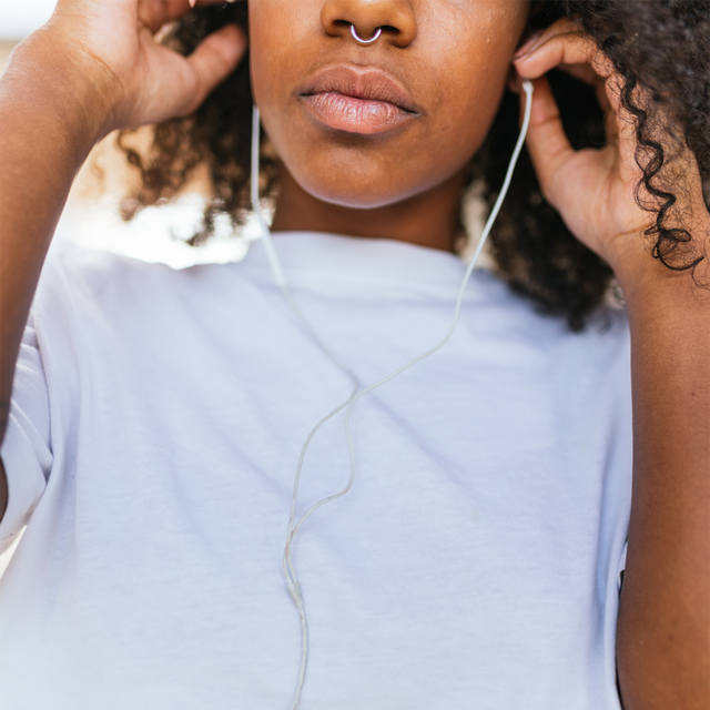 close up of a attractive african woman in white shirt and blue jeans listening to music