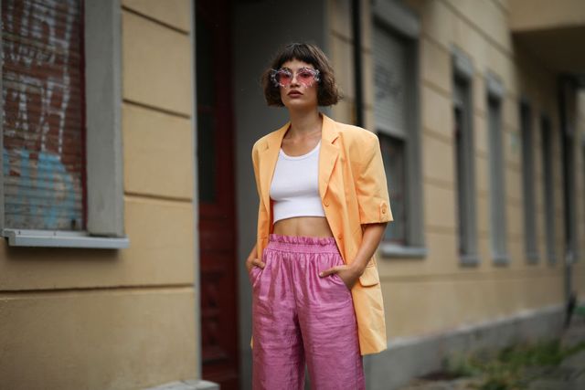 lea neumann lleva americana naranja, crop top blanco y pantalones rosa vintage y gafas de cristales rosas en berlín