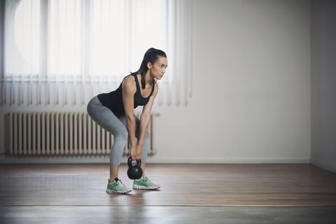 Egzersiz kıyafetleri giymiş bir kadın deadlift egzersiz hareketi yapıyor.