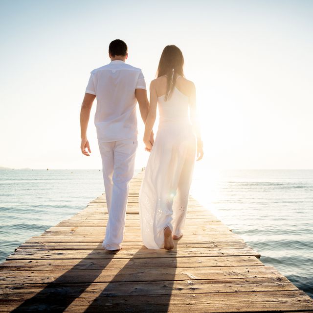 rear view of couple walking on pier in sea against sky