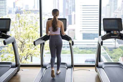rear view of fitness woman running on treadmill during a cardio session against city view in a health club