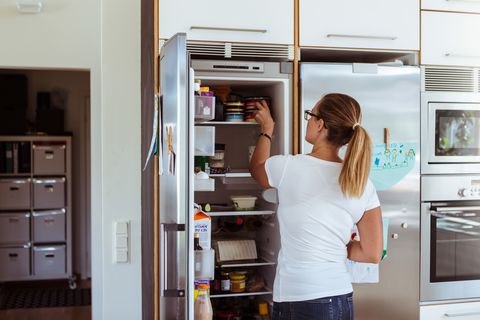 Rear view of woman looking into refrigerator while standing in kitchen