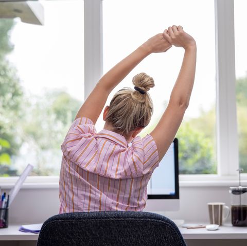 rear view of woman working from home on computer in home office stretching at desk
