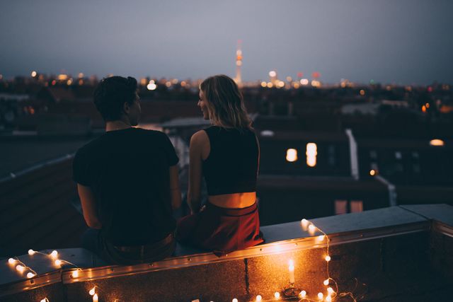 rear view of young couple sitting on illuminated terrace in city at dusk