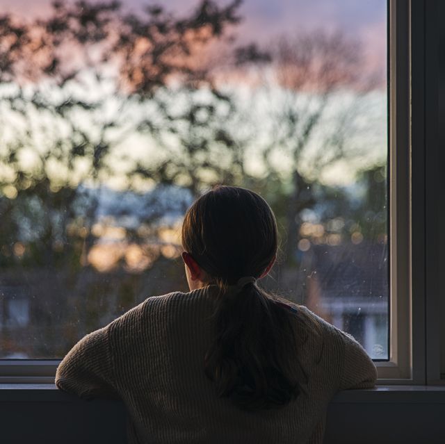 rear view shot of a young girl looking out of her window at sunset
