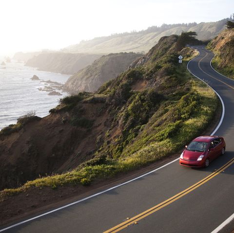 a red car driving on a winding road along the coast