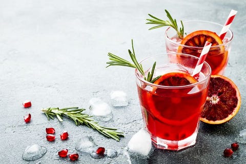 Red cocktail with blood orange and pomegranate. Refreshing summer drink on gray stone or concrete background. Holiday aperitif for Christmas party.