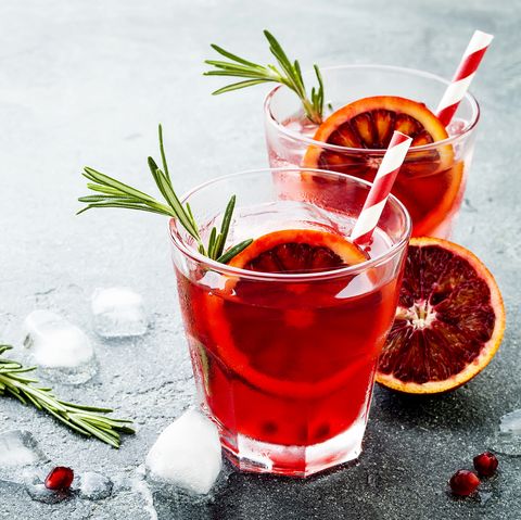 Red cocktail with blood orange and pomegranate. Refreshing summer drink on gray stone or concrete background. Holiday aperitif for Christmas party.