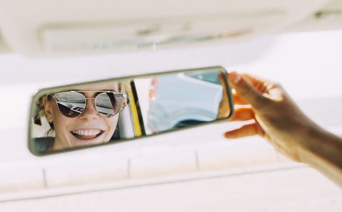 Reflection of happy young woman in rear-view mirror of a car
