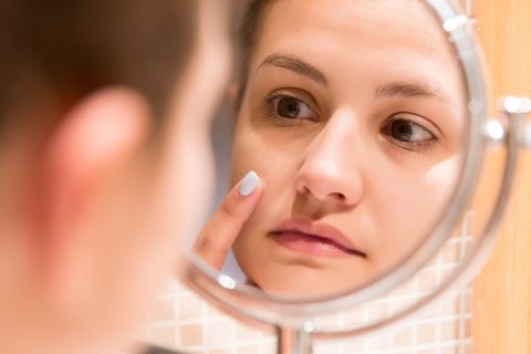 Reflection Of Woman Applying Moisturizer On Pimple In Mirror At Home