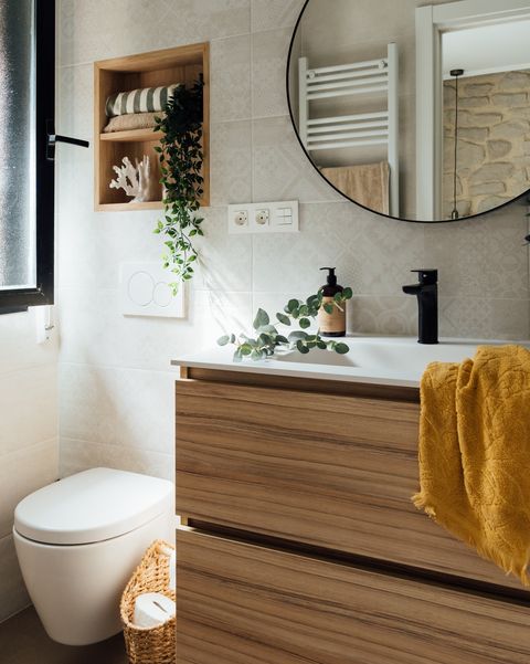 baño con mueble de madera suspendido, espejo redondo y hornacina de madera