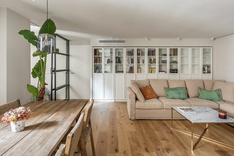 salón abierto con sofá beige, librería empotrada blanca y suelo de madera