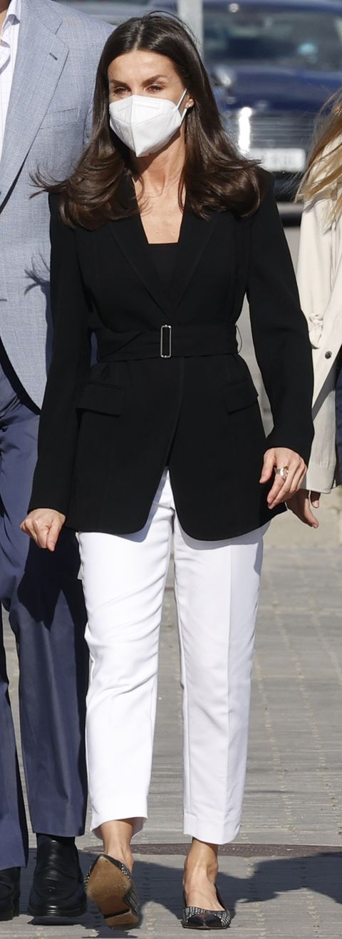 La regina Letizia, in bianco e nero, in giacca nera e pantaloni bianchi in visita con le sue figlie a un centro profughi di Madrid