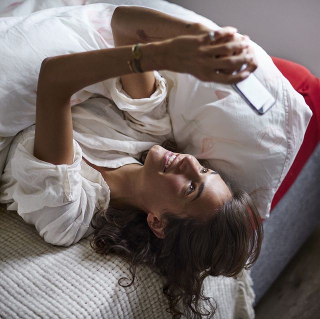 relaxed young woman using cell phone in bed