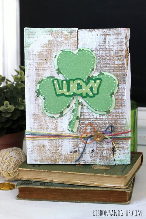 distressed looking white pallet with shamrock reading lucky and rainbow twine at the bottom tied in a bow with a gold button in the center