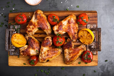 roast chicken wings on cutting board served with lemon and tomatoes