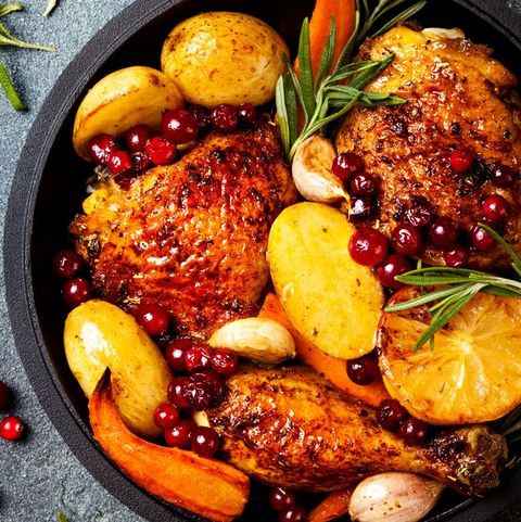 Roasted chicken legs with root vegetables, lemon, garlic, cranberry and rosemary on pan, on black slate stone background