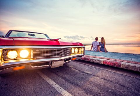 Romantic couple watching sunset with retro car