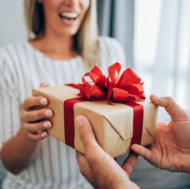 woman giving brown wrapped gift with red bow