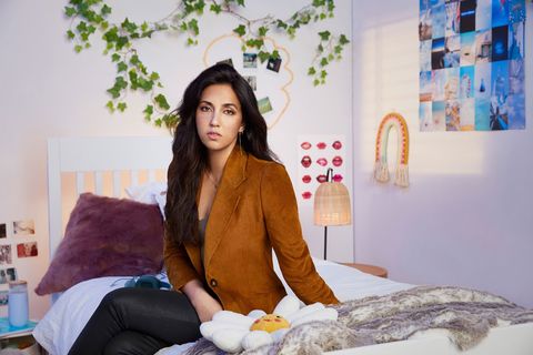 roo powell in a tan leather jacket posing on the bed of one of her decoys