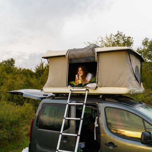 woman looking out of rooftop tent on top of car