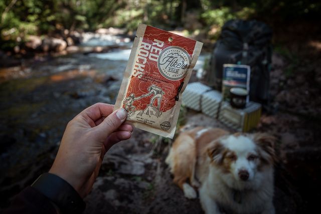 hand holding up hikers brew red rocks at camp with dog