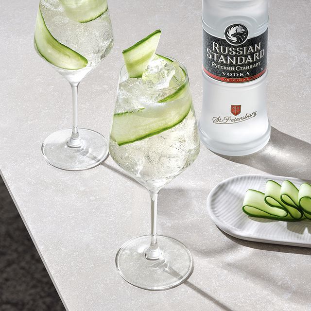 a bottle of russian standard vodka next to two glasses of vodka and ice, with cucumber garnish