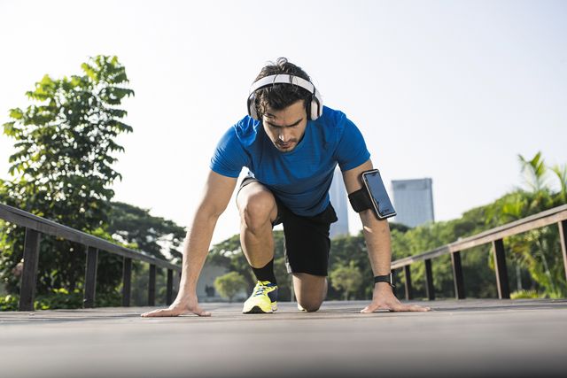 runner training start position on street in urban park, wearing headphones