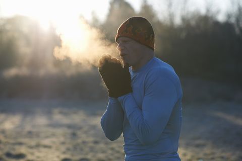 runner wearing knit hat and gloves, rubbing hands together, breathing cold air