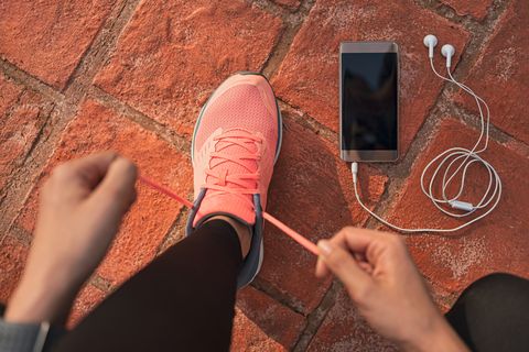 runner woman tying running shoes laces getting ready for race on run track with smartphone and earphones for music listening on mobile phone athlete preparing for cardio training feet on ground
