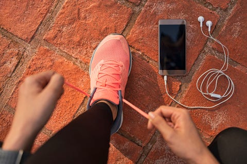 Runner woman tying running shoes laces getting ready for race on run track with smartphone and earphones for music listening on mobile phone. Athlete preparing for cardio training. Feet on ground. runner woman tying running shoes laces getting ready for race on run track with smartphone and earphones for music listening on mobile phone athlete preparing for cardio training feet on ground