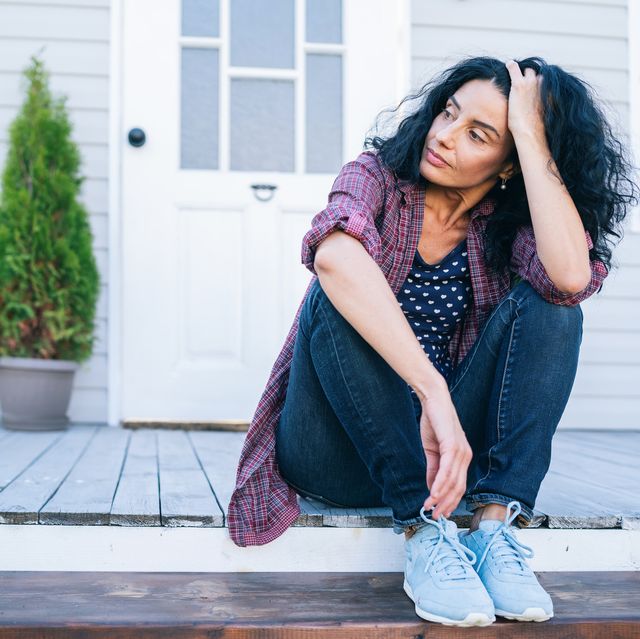 sad mid adult woman sitting on stairs in front of her house