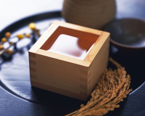 Sake in square wooden box and rice plants, high angle view, differential focus