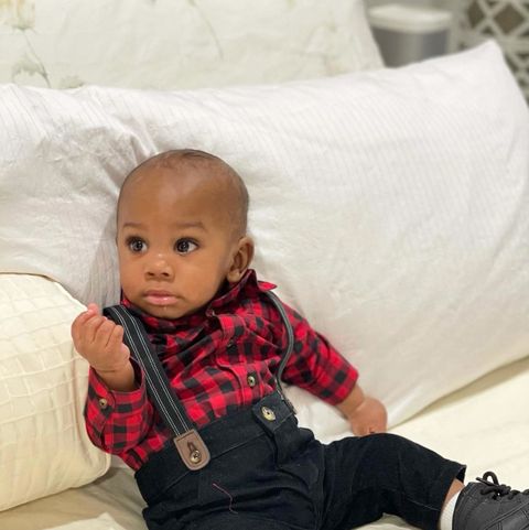baby in red checkered shit and black overalls on a bed
