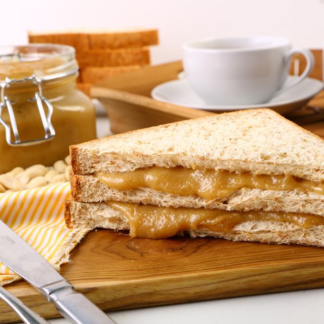 sandwich with tea cup and peanut butter on cutting board over white background