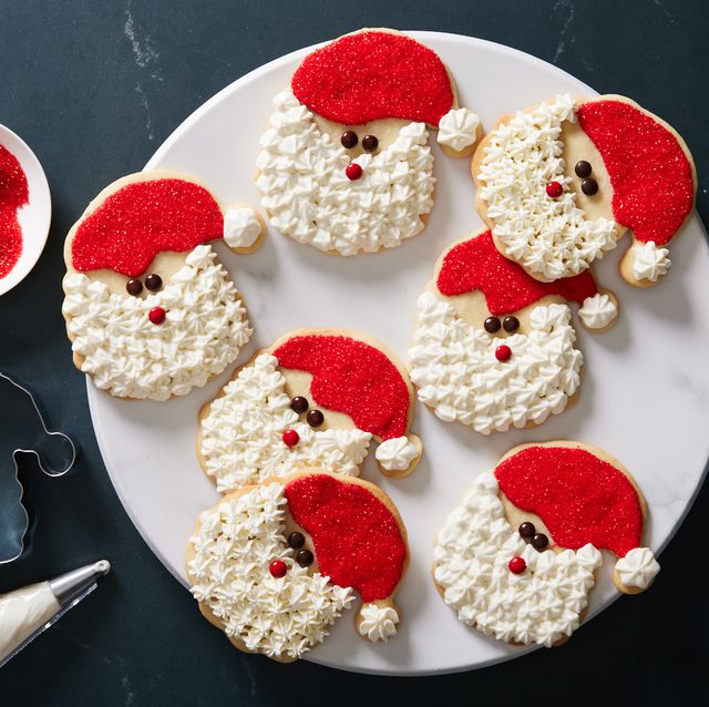 sugar cookies decorated like santa claus with white frosting, red sprinkles, and chocolate for eyes