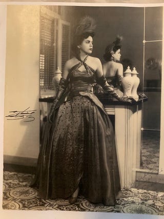 The author's mother stands against a mantel in a gown and feather-adorned headpiece. isabel gonzalez whitaker's mother sara dressed for a costume party in havana
